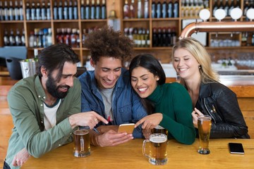Happy friends using mobile phone while having glass of beer