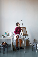 Female artist in her spacious white studio working with watercolor painting.  Natural lighting. Disclosure of creativity concept. Vertical composition with copy space