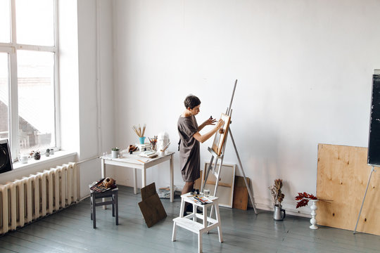 Female artist in her spacious white studio working with watercolor painting.  Natural lighting. Disclosure of creativity concept. Horizontal composition with copy space.