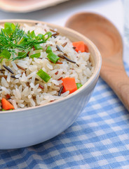 boiled mix rice in a white bowl on the white table with a wood spoon