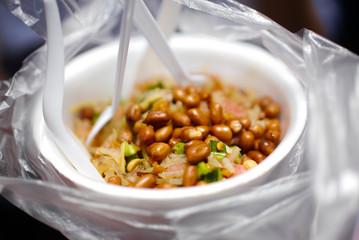 Thai Street Food - Thai Spicy Pork Skin Salad in white plastic bowl with white plastic spoons, wrapped by plastic bag
