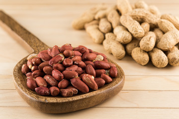 Peeled peanuts in a wooden ladle and peanuts in nutshell on a wooden table