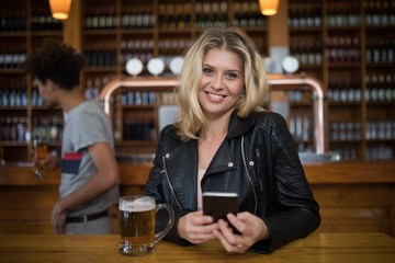 Smiling beautiful woman using mobile phone while having glass of