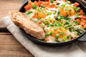 Shakshuka with eggs, tomato, and parsley in a iron pan. Shakshuka - traditional israeli tomato stew with eggs