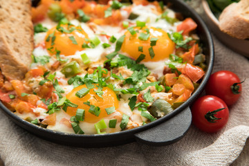 Shakshuka with eggs, tomato, and parsley in a iron pan. Shakshuka - traditional israeli tomato stew with eggs