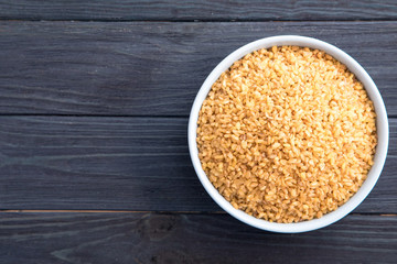 Uncooked bulgur in blue bowl on wooden table background. Dry bulgur. Spilled bulgur