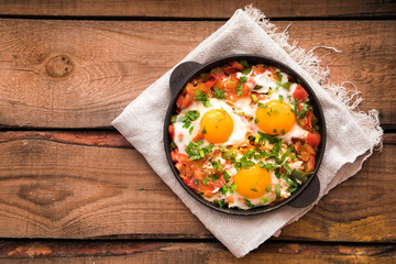 Shakshuka with eggs, tomato, and parsley in a iron pan. Shakshuka - traditional israeli tomato stew with eggs