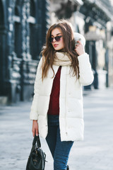 Outdoor portrait of young beautiful fashionable woman wearing stylish white winter puffer coat....