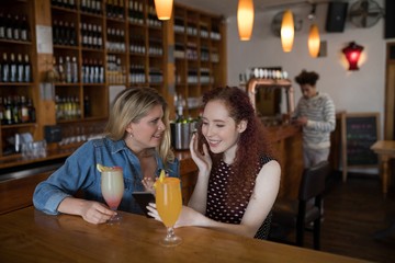 Friends gossiping over the mobile phone while sipping cocktails