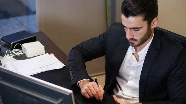 Young elegant man drawing with graphic tablet while posing at working desk.