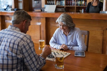 Friends playing chess while having glass of beer in bar