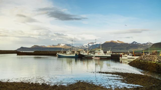 Northern Icelandic harbor port with fishing and whale watching boats and little ships and snow mountains with moving clouds at sunset