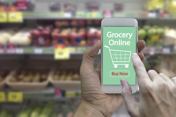 Hand use smartphone with grocery online on screen over blurred supermarket and retail store in shopping mall interior background