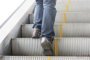 close up leg of Men wear jeans, leather shoes. Standing on the escalator