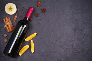 Bottle of red wine and mulled wine ingredients on black background. Spices and fruits for hot alcohol drink, copy space, top view, horizontal