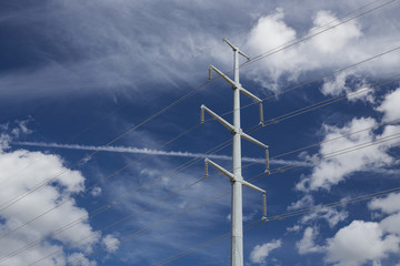 A photo of high voltage power lines with clouds and blue sky as a background