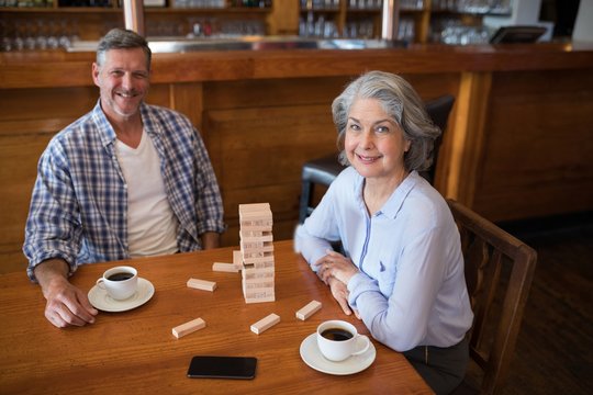 Senior friends playing jenga game on table in bar