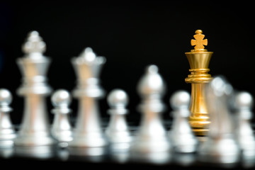 Gold king in chess game face with the another silver team on black background (Concept for company strategy, business victory or decision)