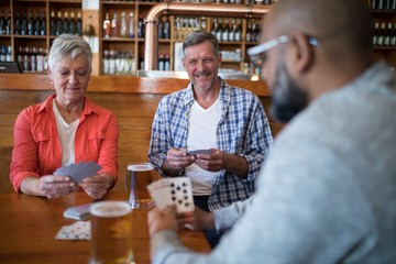 Happy friends playing cards while having glass of beer
