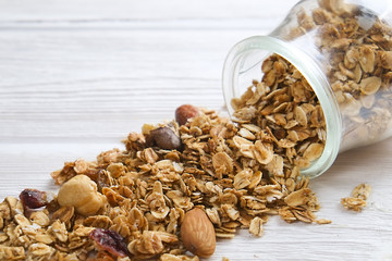 Granola superfood with almond and cashew nuts, dry fruits, raisins cherry in the glass jar on the white wooden table, top view, bright light