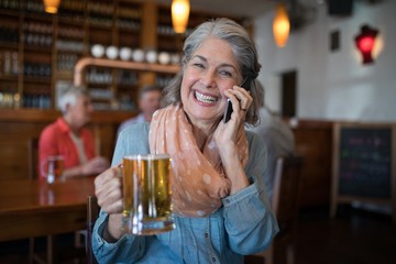 Smiling senior woman talking on mobile phone while having glass