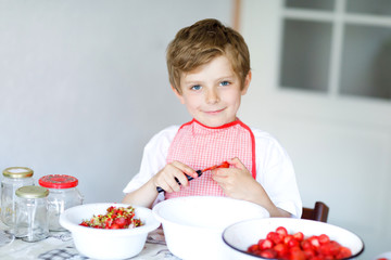 Little blond kid boy helping and making strawberry jam in summer