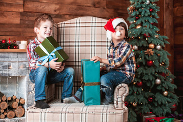 Obraz na płótnie Canvas Beautiful happy laughing children brothers play with gifts in hand in a Christmas interior with a Christmas tree. The concept of a family holiday