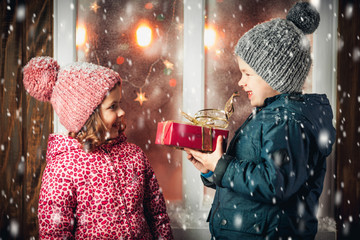 On Christmas night an adorable little boy  with his sister a girl with gifts in hand near the window the snow falls. They are waiting for Santa Claus.