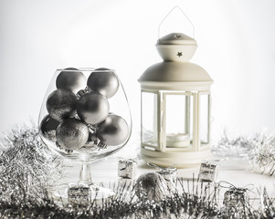 Ornaments for the new year and christmas - sparkling balls in a glass, a lantern, a candle, a tinsel on a white wooden background.