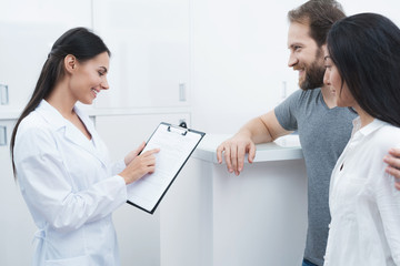 A man and a woman came to see a dentist. The receptionist fills in the form and interviews the patients.
