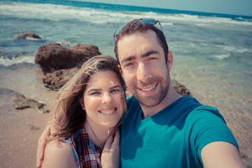 Young couple taking selfie with smartphone or camera at the beach