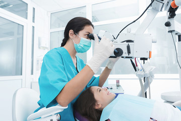 A female dentist is treating a girl. She sits on the dental chair and smiles.