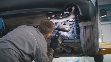 Mechanic with the lamp is checking the bottom of car in garage automobile service, close up