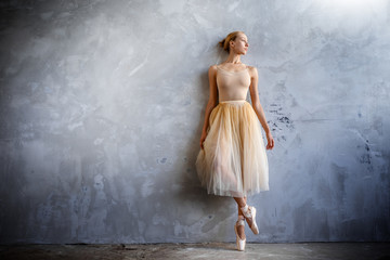 Young ballerina in a golden colored dancing costume is posing in a loft studio - obrazy, fototapety, plakaty