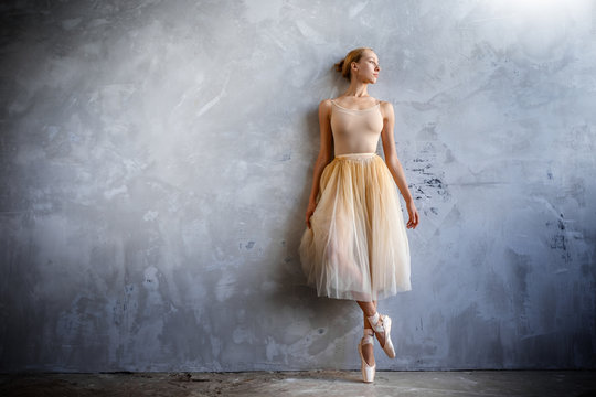 Fototapeta Young ballerina in a golden colored dancing costume is posing in a loft studio