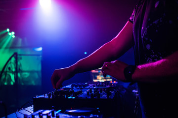 DJ in night club playing at professional mixer, color-changing spotlights