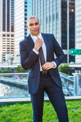 Portrait of Young European Businessman in New York. Wearing blue suit, white shirt, black tie, Mixed Race French guy with shaved head stands in business district, hands touching tie, going to work.