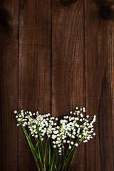 Lilies of the valley on a brown wooden background with copy space - vertical photograph.