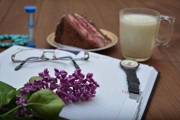 Naklejka na ściany i meble The writer's breakfast is a romantic still-life. Pencil, notebook, lilac branch, hourglass, cake and yogurt.