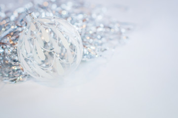 White glass decoration ball on a white background with silver tinsel behind. New Year and Christmas decoration.