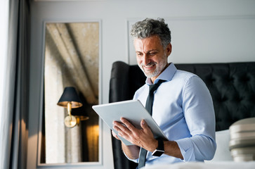 Mature businessman with tablet in a hotel room.