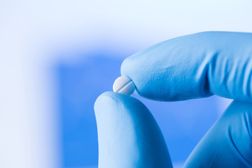 Small pill in the scientist fingers in gloves, medical research concept