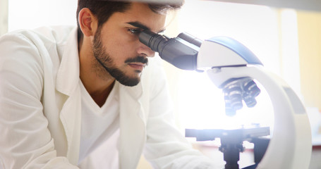 Young scientist looking through microscope in laboratory