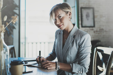 Beautiful young businesswoman writing something in note pad while sitting on armchair at living...