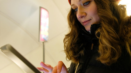 Closeup of an attractive girl with tablet in hands down the escalator in the metro, looking at the touch screen and moving your fingers across the screen