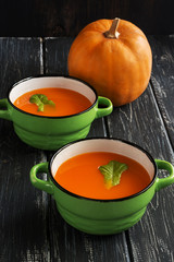 Pumpkin soup puree in green ceramic bowls on an old wooden table.