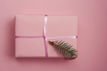 Christmas gift in a pink paper on a pink background with place for text. Flat lay. Original presentation with spruce branches