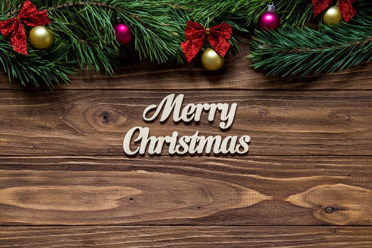 Merry Christmas on the center of the wooden background with pine tree branches on the top of the screen