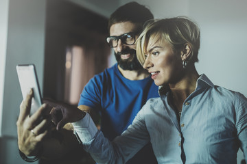 Happy family couple using smartphone in livingroom at home.Bearded man in eye glasses making selfie with young blonde woman at home. Blurred background.