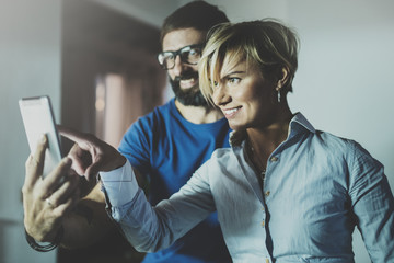 Happy family couple using smartphone in livingroom at home.Bearded man in eye glasses making selfie with young blonde woman at home. Blurred background.